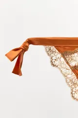 Braguita de tiro medio confeccionada en tejido satinado color naranja, con laterales ajustables mediante lazadas y detalle de encaje a contraste en los bordes.