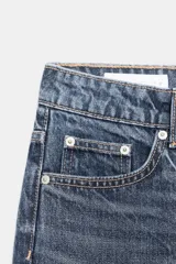 Jeans de mujer, tiro alto, color azul medio con efecto desgastado (lavado claro en muslos y oscuro en bordes). Corte recto y ancho (mom fit) con cinco bolsillos y cierre frontal de botón y cremallera.
