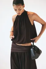 Cropped top halter de color marrón oscuro con leve brillo, escote alto con cuello elevado fruncido y diseño abullonado en el bajo.