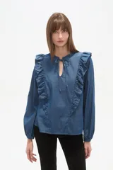 Blusa de jean con volados frontales, cuello redondo con abertura en V y lazo para anudar, y mangas largas con puños elásticos.