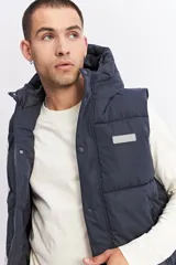 Chaleco puffer acolchado color azul marino, con capucha fija, cierre frontal con solapa de botones a presión y bolsillos laterales con cierre. Presenta un parche con el logo de la marca en el pecho.