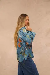 Camisa de satén azul con estampado botánico y floral en tonos amarillos, naranjas y blancos, de manga larga y cierre frontal con botones.