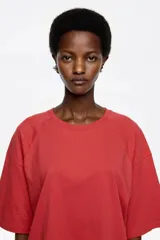Camiseta negra de corte recto y largo medio, confeccionada en algodón orgánico. Presenta escote redondo, mangas cortas amplias con costuras raglán y detalles de cortes diagonales en el cuerpo.