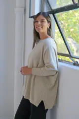 Sweater de punto con hilo lurex color beige, de corte holgado, cuello redondo y mangas largas con puños ajustados. Presenta un diseño con líneas verticales en relieve y aberturas laterales en el ruedo.