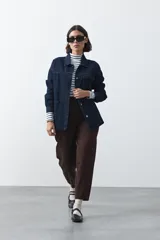 Sobrecamisa de jean color negro con silueta relajada, cuello camisero, cierre frontal con botones metálicos, bolsillos frontales y cinturón ajustable en la cintura.