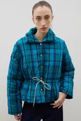 Campera puffer de corte corto con diseño a cuadros en tonos turquesa y azul. Presenta cuello alto, cierre frontal con botones a presión y cintura ajustable mediante cordón con ajuste de frunce.