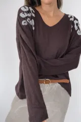 Buzo de punto oversize con cuello en V, confeccionado en tejido suave con detalles de piedras plateadas en los hombros que forman un diseño tipo print. Presenta un calce holgado y mangas largas.