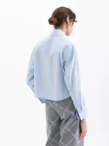 Camisa de corte recto y holgado, color celeste, con cuello clásico, cierre frontal con botones y mangas largas con puños abotonados.