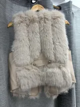 Chaleco sin mangas de piel sintética con diseño de pelo largo, forro interior y detalle de hebilla lateral. Presenta un corte abierto al frente.