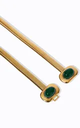 Cinturón fino de metal dorado con diseño minimalista y flexible. Presenta un detalle central decorativo con dos piedras verdes engarzadas y cierre ajustable.