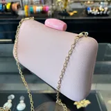 Clutch de rafia sintética color rosa suave, con cierre a tono y asa desmontable de cadena dorada. Incluye borla decorativa.