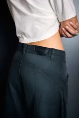 Pantalón de jean color gris oscuro, de corte holgado y diseño con costuras frontales verticales. Presenta una cintura de tiro medio y un detalle de mosquetón metálico con dije colgante en la parte frontal.