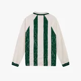Camiseta de manga larga estilo jersey de fútbol, con diseño a rayas verticales alternando blanco y encaje verde. Presenta cuello polo con detalles en blanco y verde, y un escudo circular bordado en el centro del pecho con una rosa.