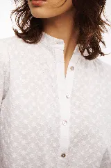 Camisa blanca de algodón bordado con motivos florales, cuello mao, botones al frente y terminación con bordes redondeados.