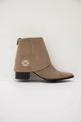 Bota de caña corta confeccionada en cuero color chocolate, con punta fina y taco cuadrado. Presenta una polaina desmontable que cubre el tobillo, decorada con un bordado sutil en el lateral.