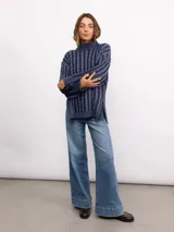 Sweater de punto con diseño de trenzas verticales, cuello alto y silueta oversize. Presenta un patrón bicolor en tonos azul y azul oscuro, con mangas largas y terminaciones en tejido acanalado.