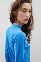 Remera de cuello alto y manga larga en color crudo, con costuras a la vista en contraste de color marrón.