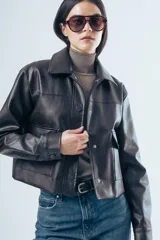 Chaqueta de cuero sintético en color marrón oscuro, con cuello clásico, cierre frontal con botones a presión y dos bolsillos aplicados en el pecho. Presenta un corte recto y estructurado.