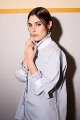 Camisa celeste a rayas verticales azules y marrones, con cuello blanco, cierre frontal con botones dorados y volantes verticales.