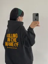Hoodie canguro con cierre frontal, color negro con efecto acid wash, con capucha y bolsillos tipo canguro. Presenta el texto estampado en amarillo "Now You Do What They Told Ya" en el pecho.