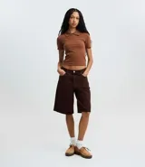 Blusa polo beige de manga corta, confeccionada en tejido canelado de rib de algodón con elastano, que proporciona un ajuste cómodo y una caída ajustada.