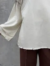 Buzo oversize de color crudo con diseño de costuras expuestas en contraste y terminaciones desflecadas en mangas y ruedo. Presenta un corte holgado con mangas anchas.