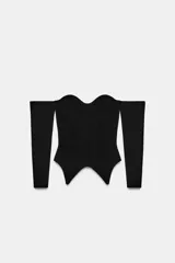 Top corsetero de punto color negro, con escote recto, hombros descubiertos, manga larga y bajo asimétrico.