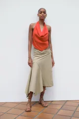 Top de color naranja vibrante con cuello halter que se anuda en la espalda, creando un escote drapeado o fluido en el frente. El bajo del top tiene un corte en pico con tiras finas colgantes.