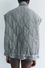 Chaleco gris acolchado con cuello alto, cierre frontal con cremallera metálica, bolsillos de plastrón en delantero y bajo ajustable con cordones.