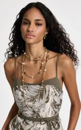 Collar largo de diseño en capas, elaborado en metal con acabado dorado. Presenta una estructura de cadena fina intercalada con aplicaciones de perlas blancas y piedras cuadradas en tonos rojizos y oscuros.