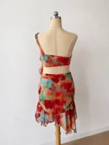 Vestido corto de dos piezas (crop top y minifalda) con estampado abstracto en tonos rojos, naranjas, amarillos y azules. El top es tipo bandeau con un tirante que incorpora un volante drapeado que cae sobre el abdomen. La minifalda es ajustada con volante en el ruedo.