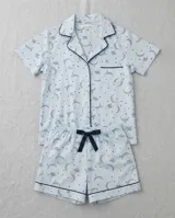Pijama de algodón color celeste, compuesto por una camisa de manga corta con botones y un short con elástico en la cintura, ambos con detalles de ribetes oscuros y estampado de lunas y estrellas.