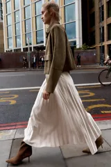 Falda midi plisada de tiro alto color beige, con cinturón a tono y hebilla metálica dorada. Cierre lateral con cremallera oculta.