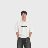 Remera polo blanca de manga corta, con cuello solapa, cierre frontal parcial de botones ocultos y estampado tipográfico "VenefoClub" en el pecho.