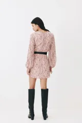 Vestido corto de gasa arrugada en color rosado con estampado floreado, escote en V y costura fruncida central con botones decorativos forrados. Cuenta con mangas globo largas con puños elásticos y cierre oculto en la espalda.