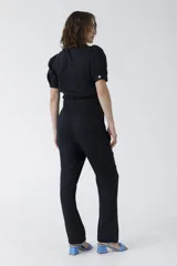 Mono negro de lino con escote pronunciado en V y nudo frontal que deja ver un corte en la cintura. Mangas cortas abullonadas y pantalón de corte recto.