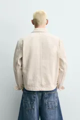 Cazadora cropped fit confeccionada en tejido de algodón con estructura diagonal de color beige, cuello solapa, manga larga y cierre frontal con cremallera. Cuenta con bolsillos de plastrón con solapa en el pecho.