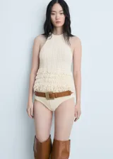 Top tejido de punto color crudo, con cuello halter y detalle de flecos en el ruedo.