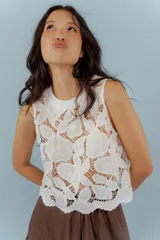 Blusa sin mangas color blanco, con cuello redondo y confeccionada completamente en tejido de encaje con motivos florales.