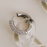 Aros colgantes compuestos por una argolla de plata 925 con incrustaciones de cristales y un dije de cadena de eslabones de vidrio transparente.