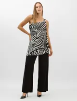 Enterito de seda fría con pantalón palazzo de corte ancho y fluido. Presenta un diseño asimétrico con una tira fina en un hombro y un detalle de herraje metálico en el otro, del cual se desprende una capa de gasa estampada con patrón abstracto en blanco y negro.