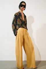 Jeans de tiro bajo y corte wide leg, color amarillo mostaza, con pliegues frontales, bolsillos ocultos y cierre frontal con cremallera, botón y ganchos metálicos.
