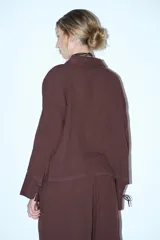 Camisa de manga larga color crema o beige claro, con textura arrugada, cuello camisero y cierre frontal mediante lazos anudados.