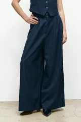 Pantalón sastre de corte wide leg y tiro alto, en color beige. Presenta pinzas frontales, cierre con botón y bolsillos laterales.