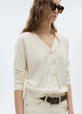 Cardigan de punto fino en color crudo, con cuello en pico y cierre frontal de botones. Presenta un diseño recto de manga larga con puños y ruedo acanalados.