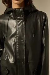 Pilot de efecto cuero negro con acabado brillante, diseño de manga larga, capucha con cordones ajustables y cierre frontal con botones a presión. Cuenta con bolsillos laterales con solapa.