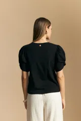 Remera blanca de cuello redondo con mangas cortas abullonadas y detalle de nudo en los puños.