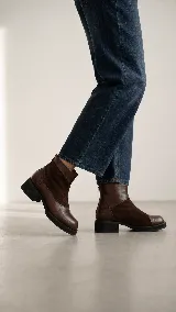 Bota corta de cuero color marrón, con diseño de texturas combinadas, talón con textura grabada, taco geométrico y cierre lateral.