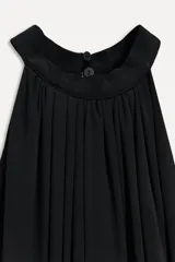 Vestido midi negro con cuello halter, hombros descubiertos, cintura elastizada, detalle de drapeado lateral y bajo asimétrico. Cierre con botones en el cuello.