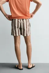 Bañador de hombre con estampado de rayas verticales anchas en tonos marrón oscuro y beige claro, con finas líneas rosadas entre ellas. Posee cintura elástica con cordón ajustable y forro interior.